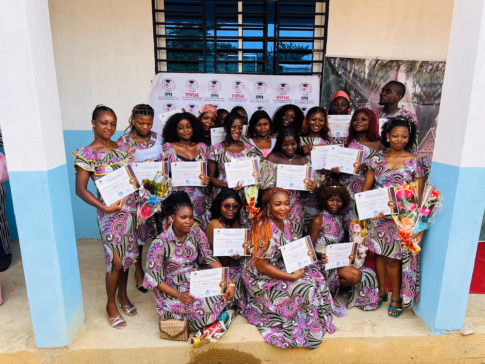 Une promotion de diplômées en tenue traditionnelle assortie pose avec ses attestations devant la banderole aux logos EFOPSAB et IFPPB.