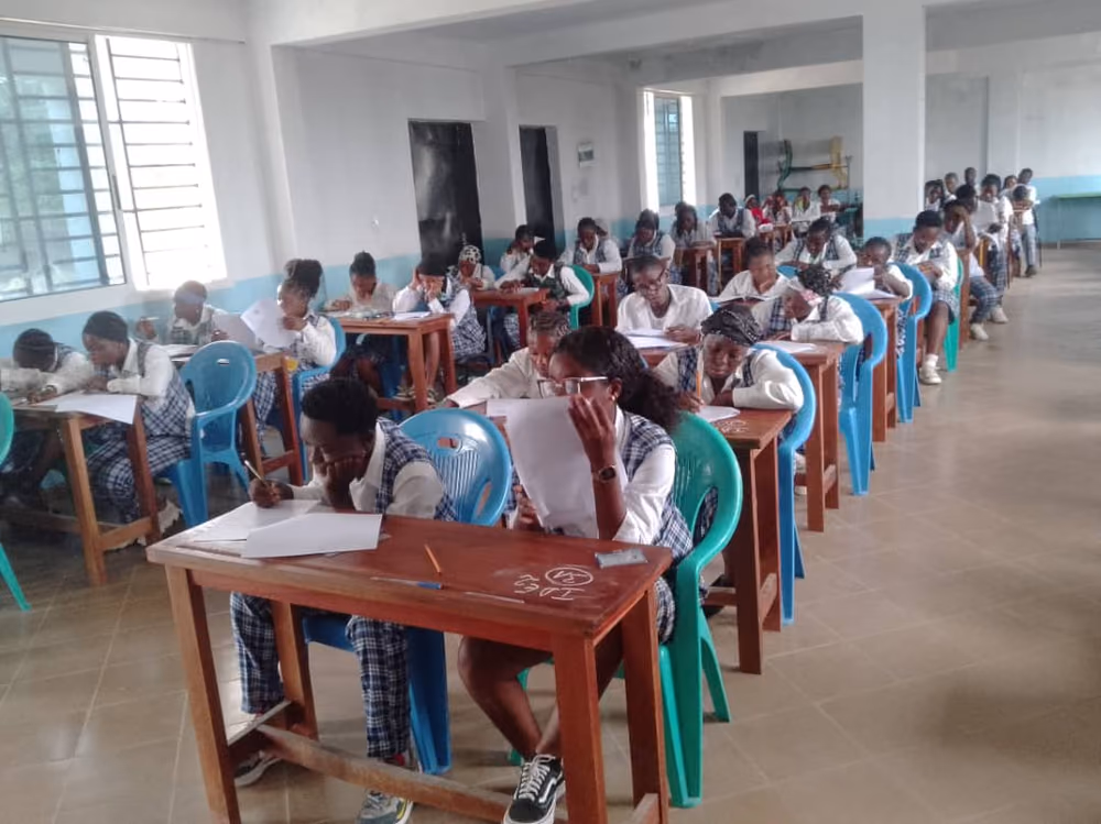 Vue en enfilade d'une salle d'examen, les étudiantes penchées sur leurs copies.