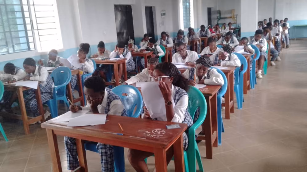 Vue en enfilade d'une salle d'examen du campus, les étudiantes penchées sur leurs copies.